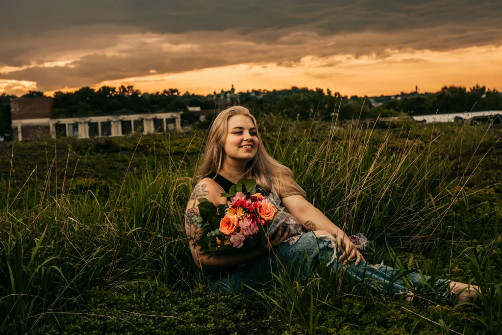 A person holds flowers while standing in a field of tall grass.