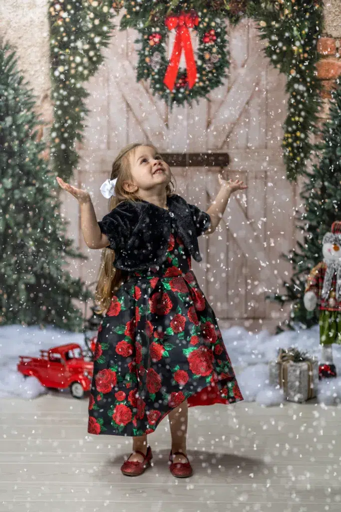 A person stands in front of a Christmas tree wearing a dress.