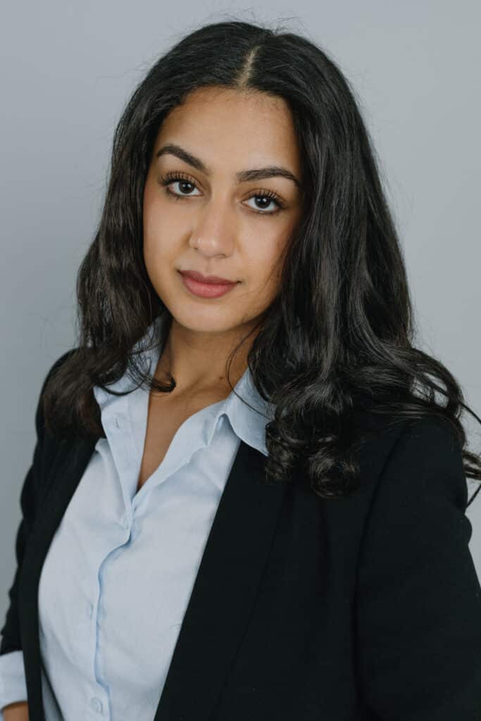 A person is wearing a fashionable coat and makeover while posing for a headshot portrait with layered hair, long eyelashes, and a bold lip color.