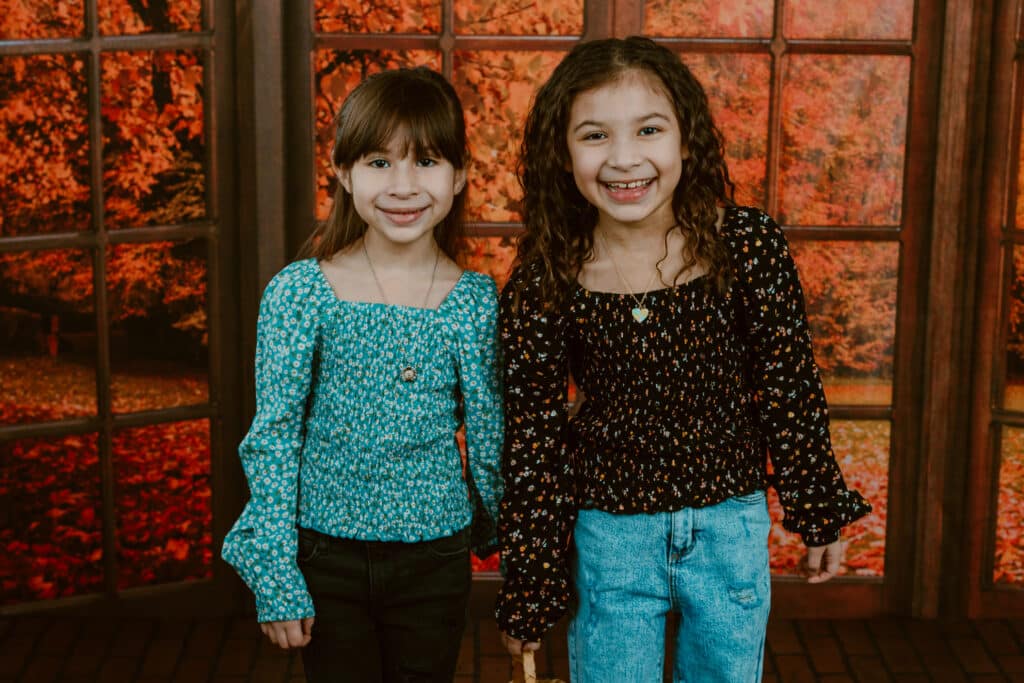 A young person is posing with a smiling toddler in jeans indoors.