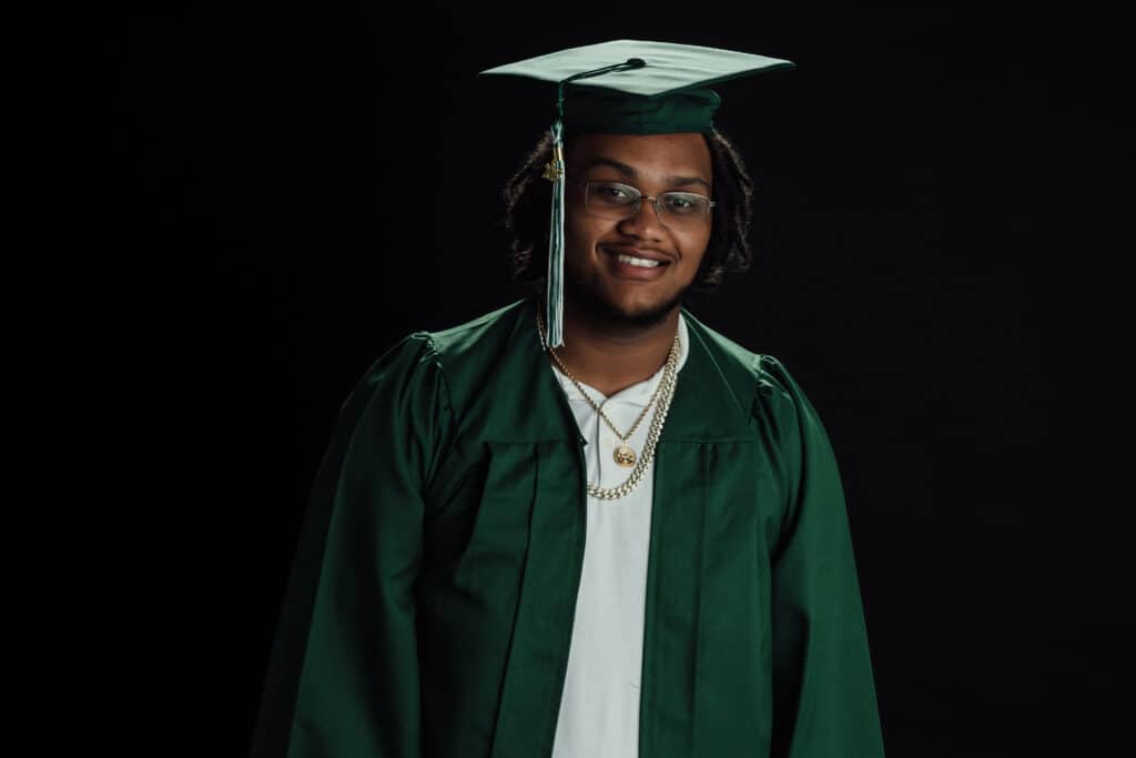 A person wearing a mortarboard and academic dress is smiling while holding a diploma, signifying their graduation commencement.