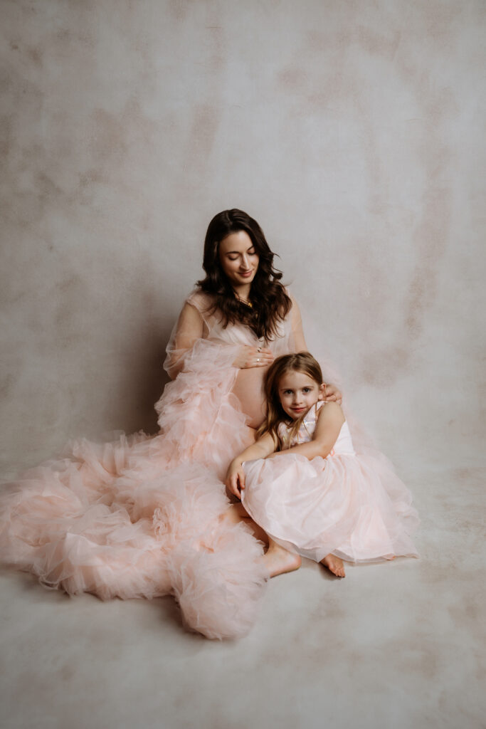 A person and child sitting on a soft, fabric-draped floor. Both wear elegant, light pink dresses, creating a serene atmosphere.