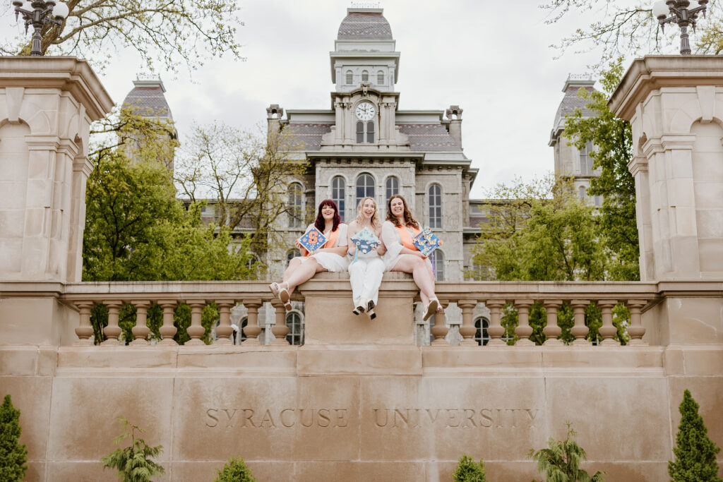 Three smiling people are sitting atop a stone wall engraved with