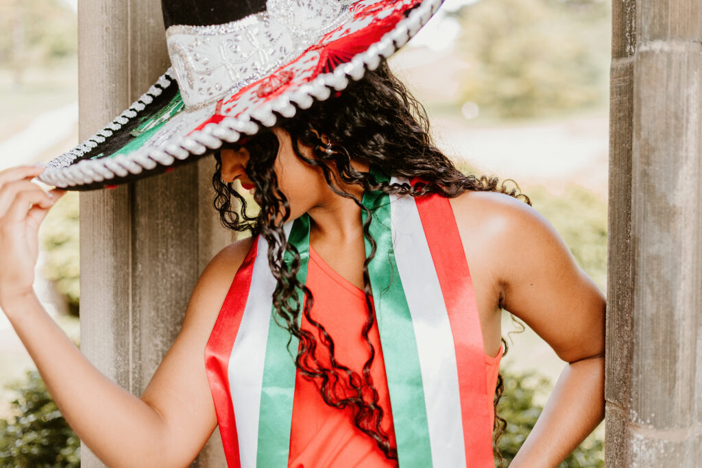 A person wears a large sombrero with the Mexican flag's colors—red, white, and green—and a matching sash, partially obscured, outdoors near a column.