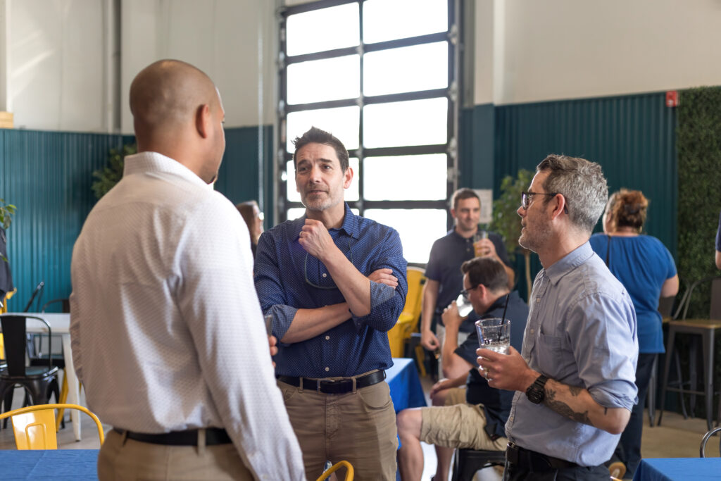 A group of people socialize in a modern, industrial-style room with large windows and blue decor.