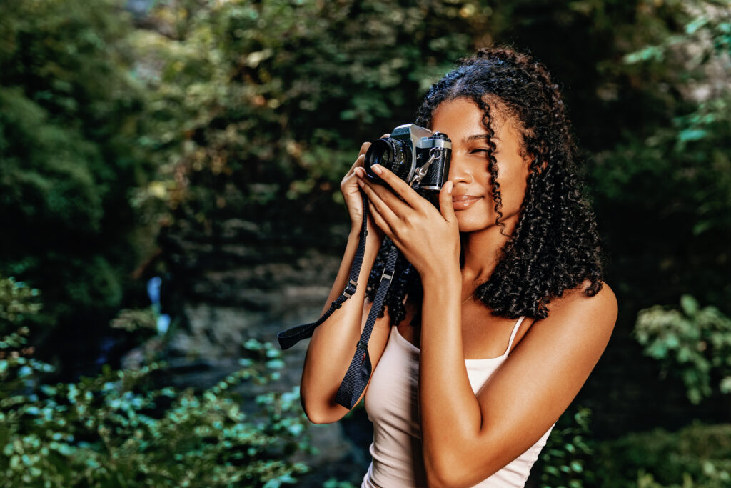 A person is taking a photo with a vintage camera in a lush, green outdoor setting. No recognizable landmarks or historical buildings are visible.