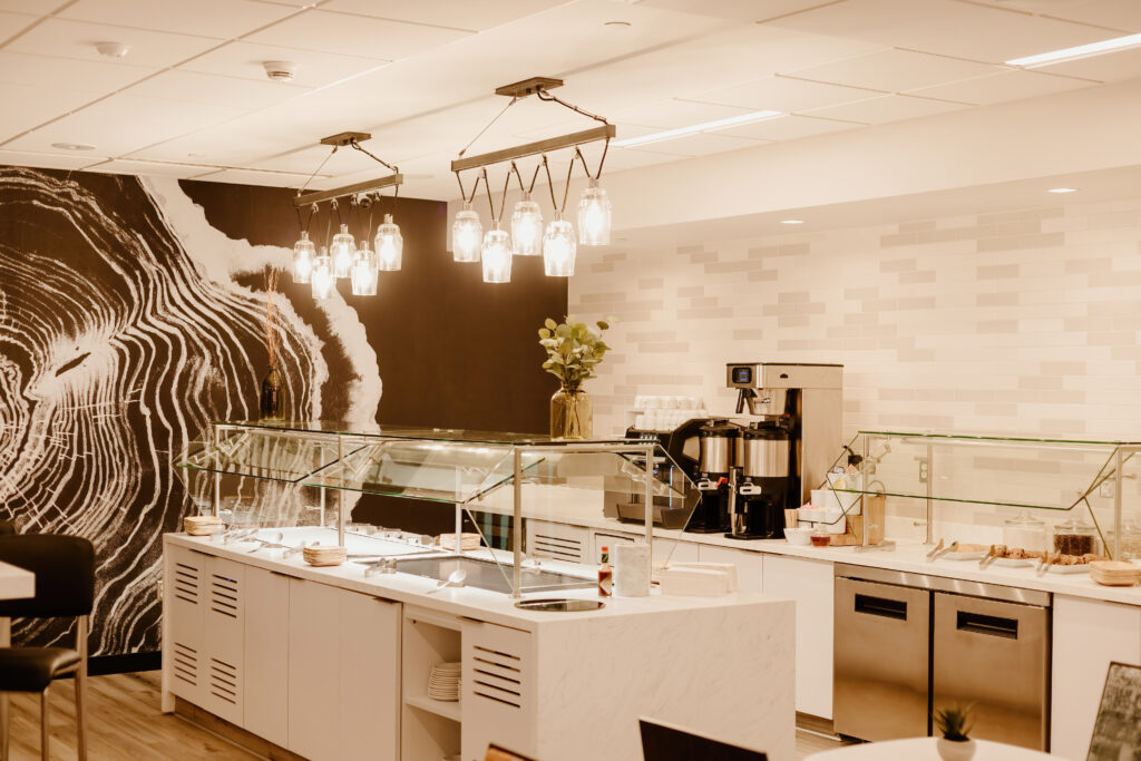 A modern cafeteria with white and black decor, featuring glass display counters, a coffee machine, and unique tree-ring artwork on the wall.