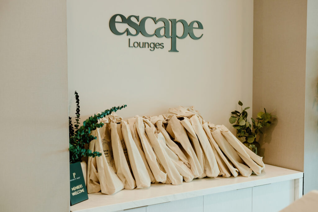Display at Escape Lounges showing bags and green plants. A sign says,