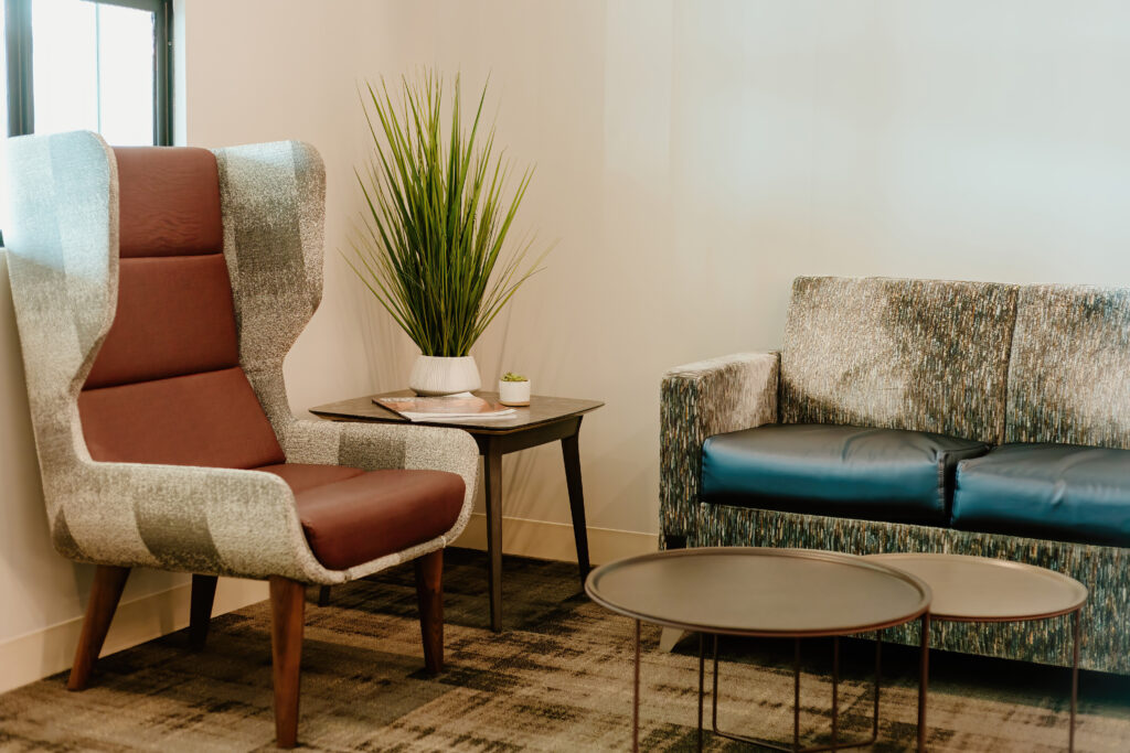 Modern lounge area featuring a cozy armchair, stylish sofa, side table with plants, and round nested coffee tables on a patterned carpet.