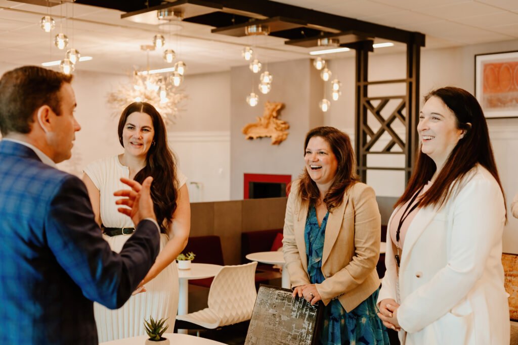 Four people in a modern office setting engaged in conversation, with stylish lighting and contemporary decor in the background.