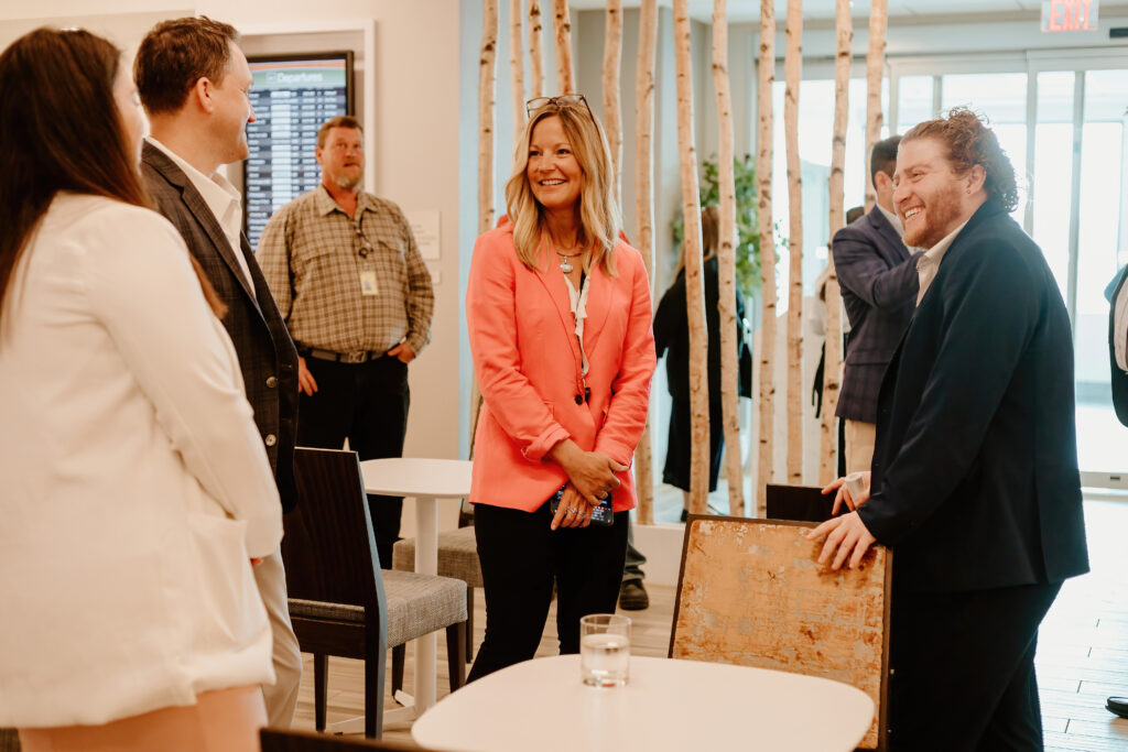 Four people engaged in conversation in a modern room with a departures board and wooden decor elements in the background.