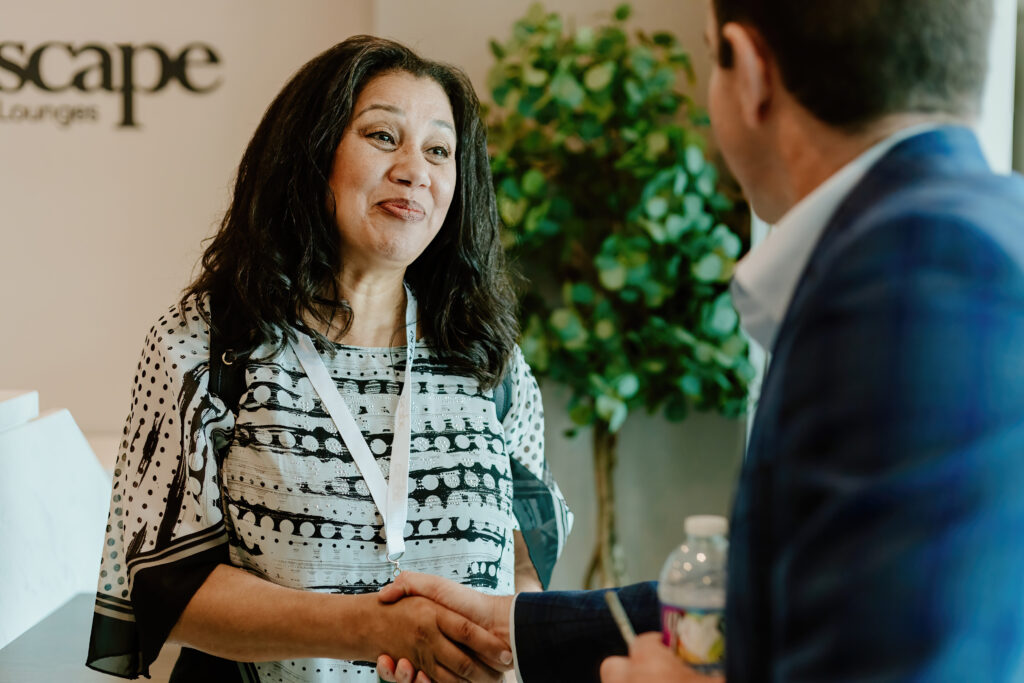Two people exchange handshakes in a professional setting. A person in patterned clothing faces another holding a water bottle.