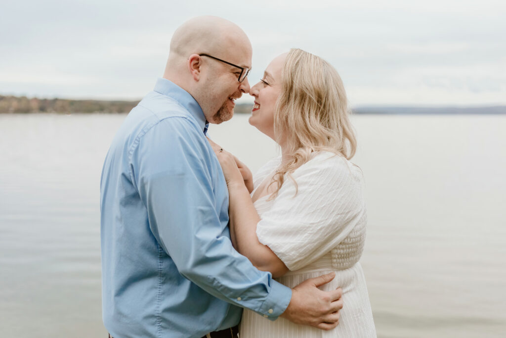 Two smiling people embrace by tranquil waters, in close, affectionate contact, exuding a sense of warmth, connection, and happiness against a nature backdrop.
