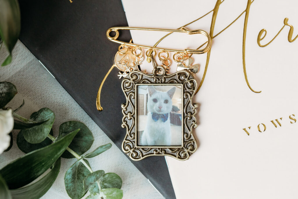 Ornate vintage frame pendant with a small photo of a cat, resting on a light surface beside greenery.