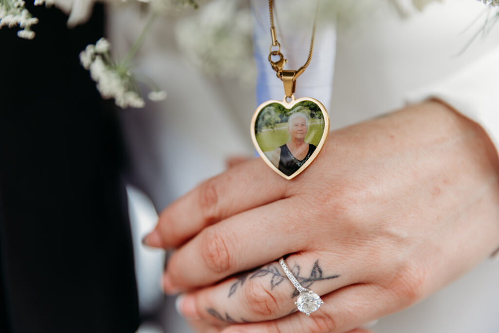 Close-up of hands displaying a diamond engagement ring and a heart-shaped photo pendant necklace.