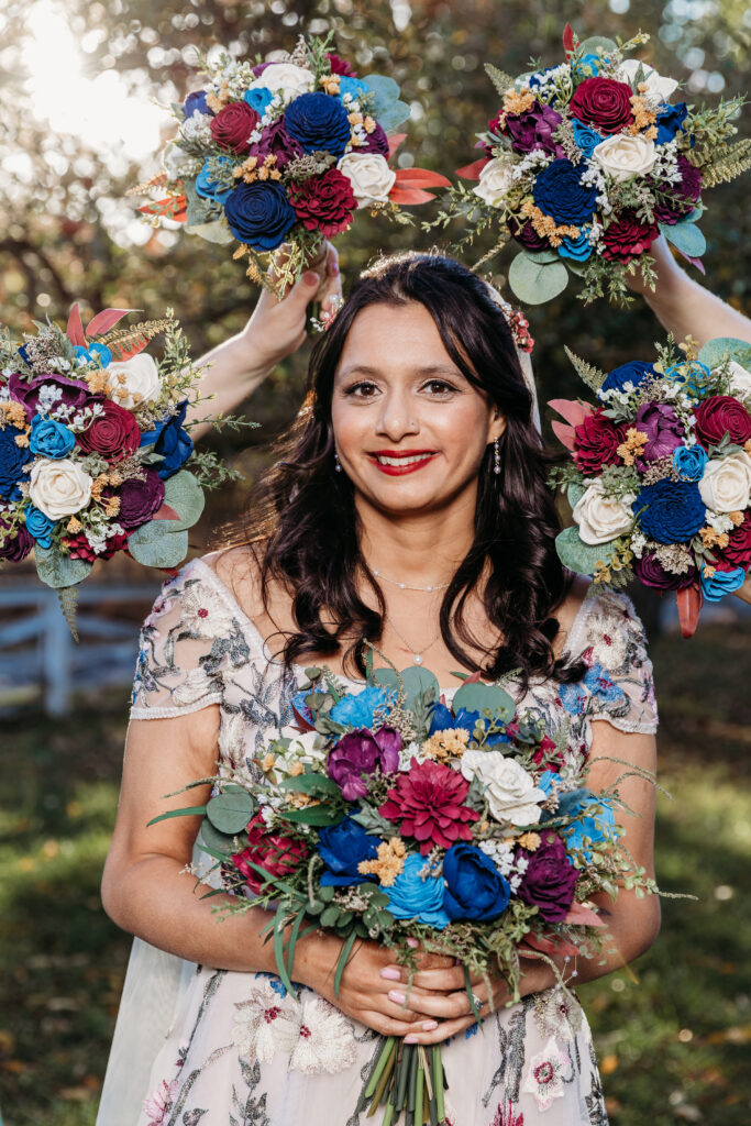 Smiling woman in a floral dress holds a colorful bouquet outdoors, with additional bouquets raised around her.