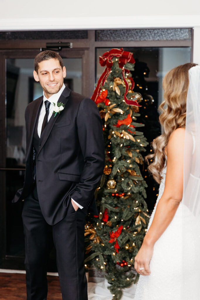 Two people are in formal attire, standing near a decorated Christmas tree. One person wears a veil, suggesting a wedding setting.