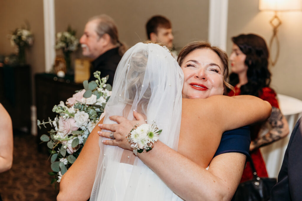 Bride in a white veil hugs a woman in a blue dress at a wedding reception.