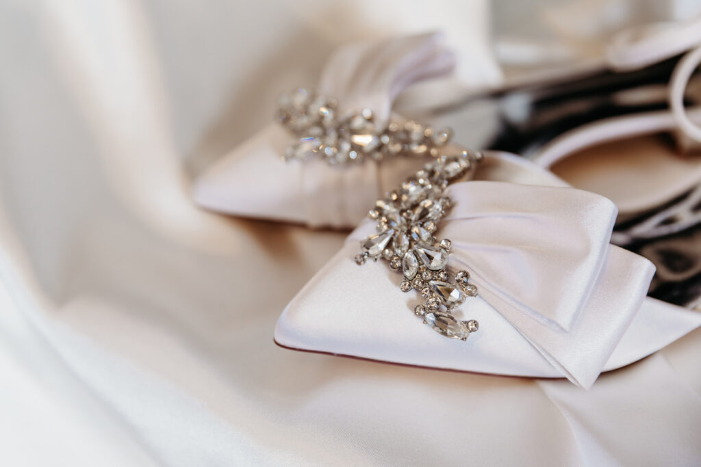 Elegant white satin shoes adorned with intricate crystal embellishments, resting on a soft, flowing fabric background.