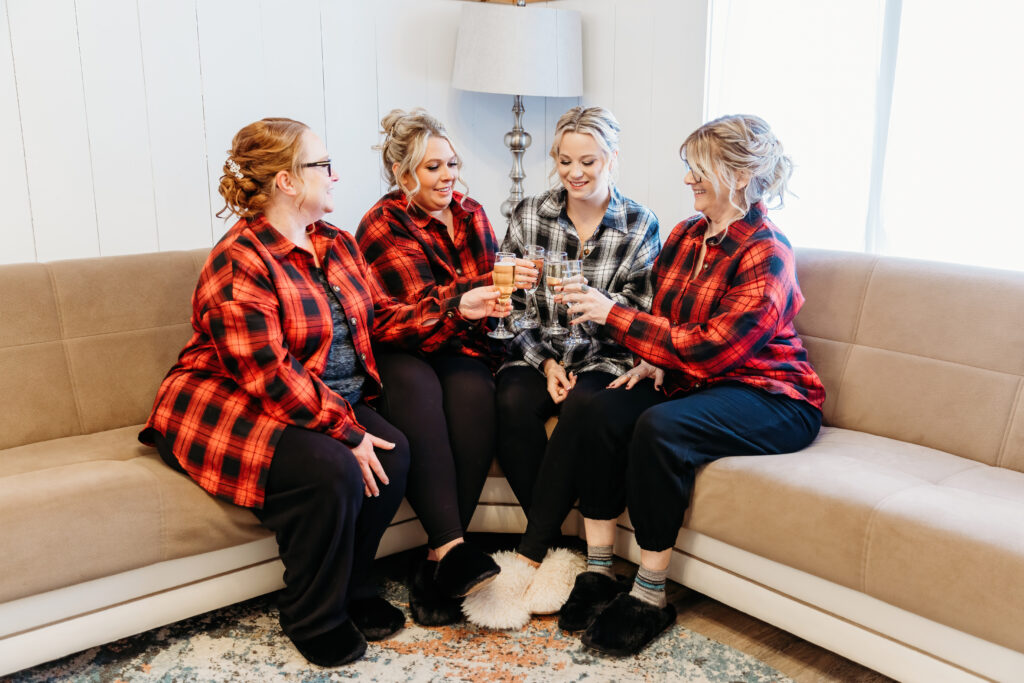 Four persons in plaid shirts sit on a couch, toasting with drinks, in a cozy, well-lit living room.
