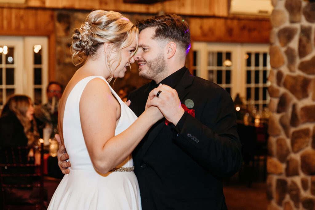 Two people dancing closely at an indoor event, surrounded by warm lighting and stone accents, with people seated in the background.