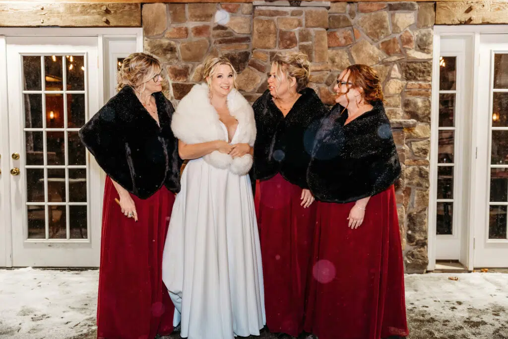 Four people in formal attire stand outside a brick building, with two glass doors and snow on the ground.