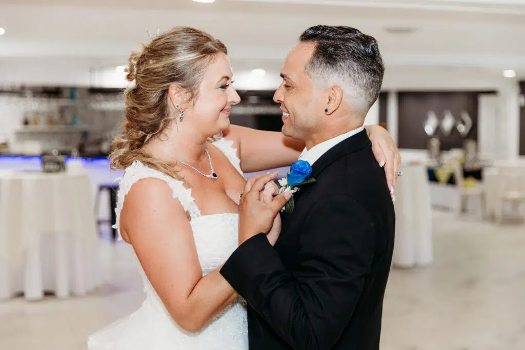 Two people in formal attire are joyfully interacting at a wedding reception, with elegant decorations and a bar area in the background.