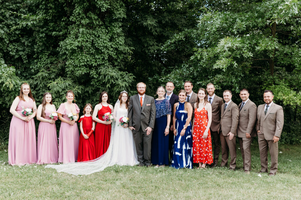 This image features a group of formally dressed people smiling for a photo at an outdoor setting with lush greenery in the background.