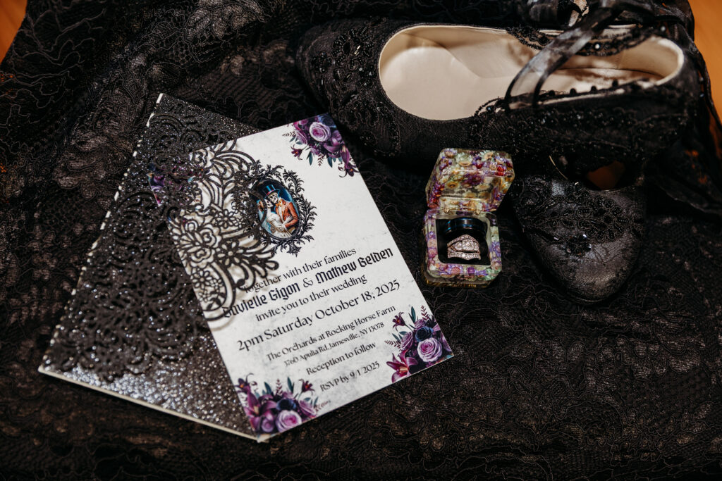 Ornate invitation cards with floral filigree designs on black lace, beside a small jeweled box and a beige high-heeled shoe.
