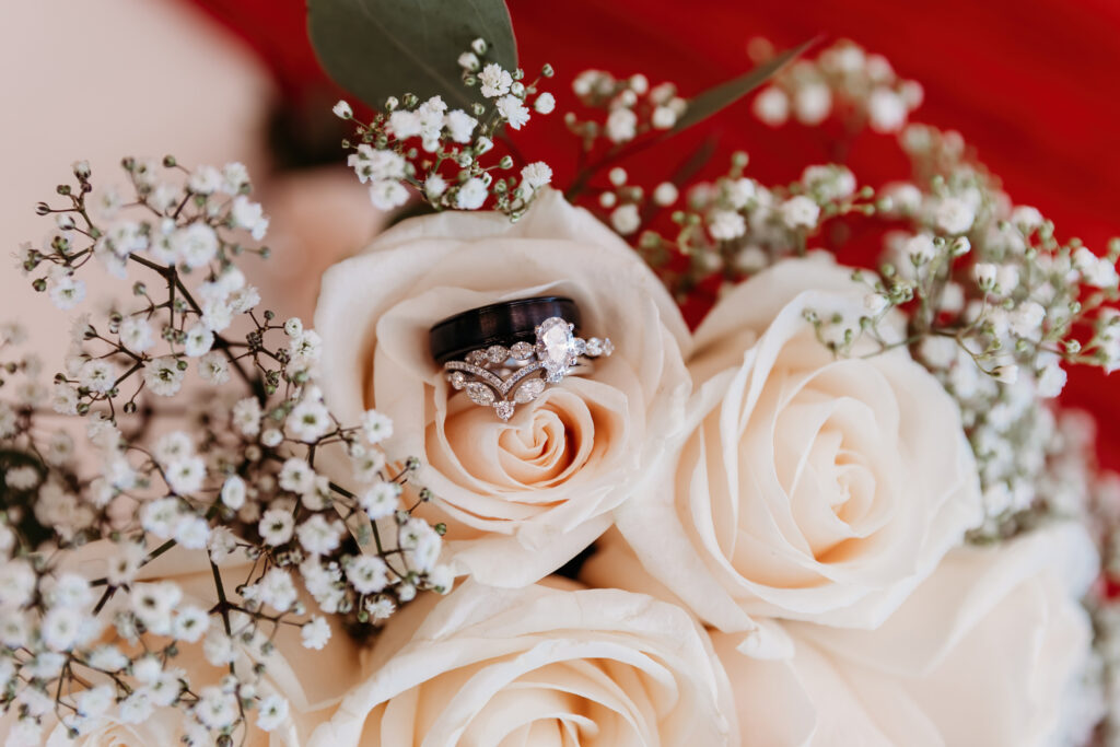 A bouquet of white roses with two rings nestled in the center, surrounded by baby's breath flowers.