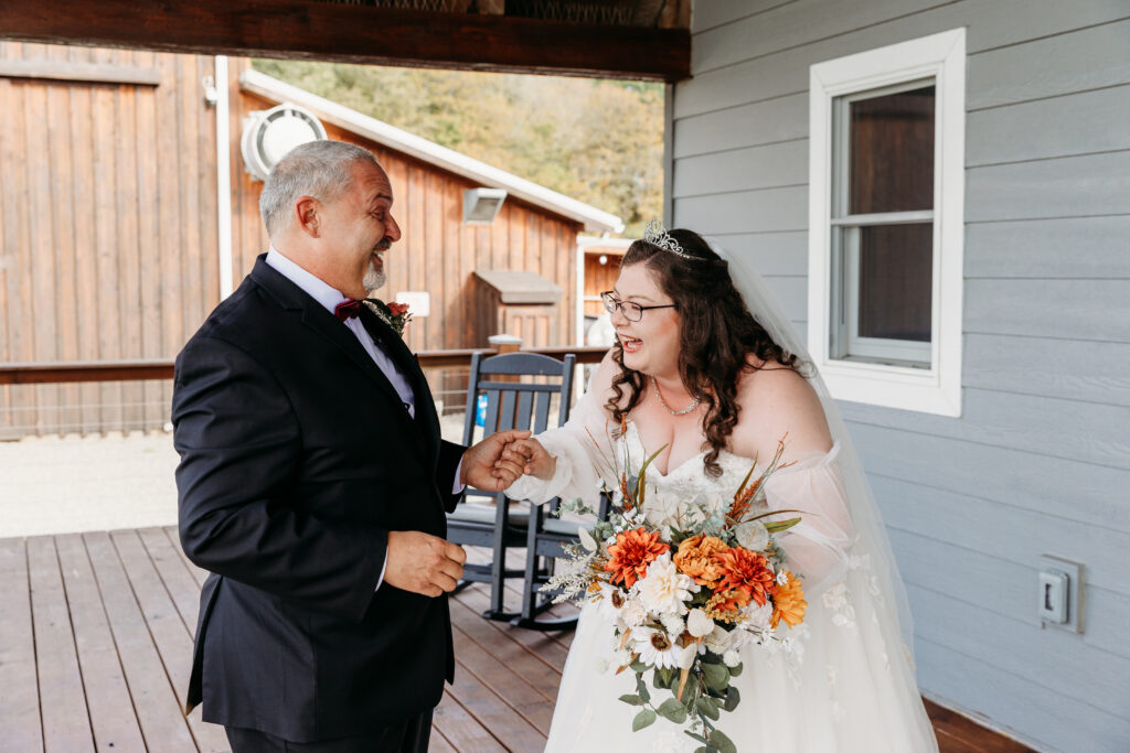 Bride in a white wedding dress holding a bouquet shakes hands with a man in a dark suit on a wooden porch.