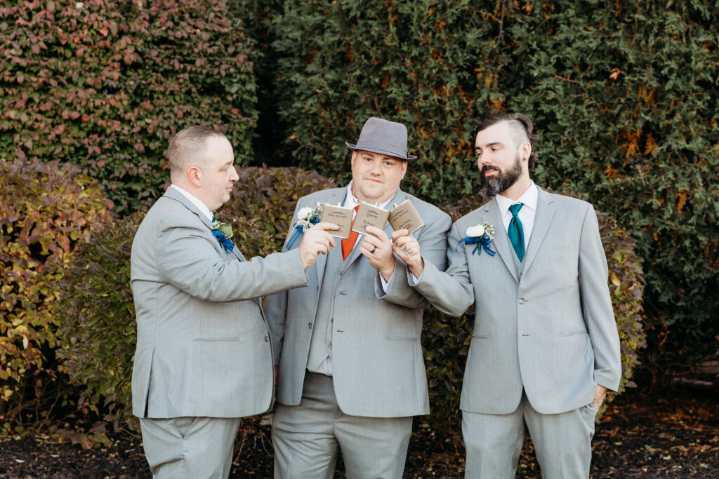 Three people in suits hold small booklets, posing together outdoors in front of lush greenery and bushes, creating a formal and cheerful atmosphere.