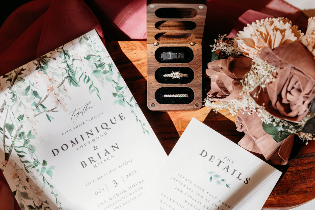 Flat lay of wedding invitations featuring floral details and a “Details” card, placed with pink roses and decorative elements on a wooden surface.