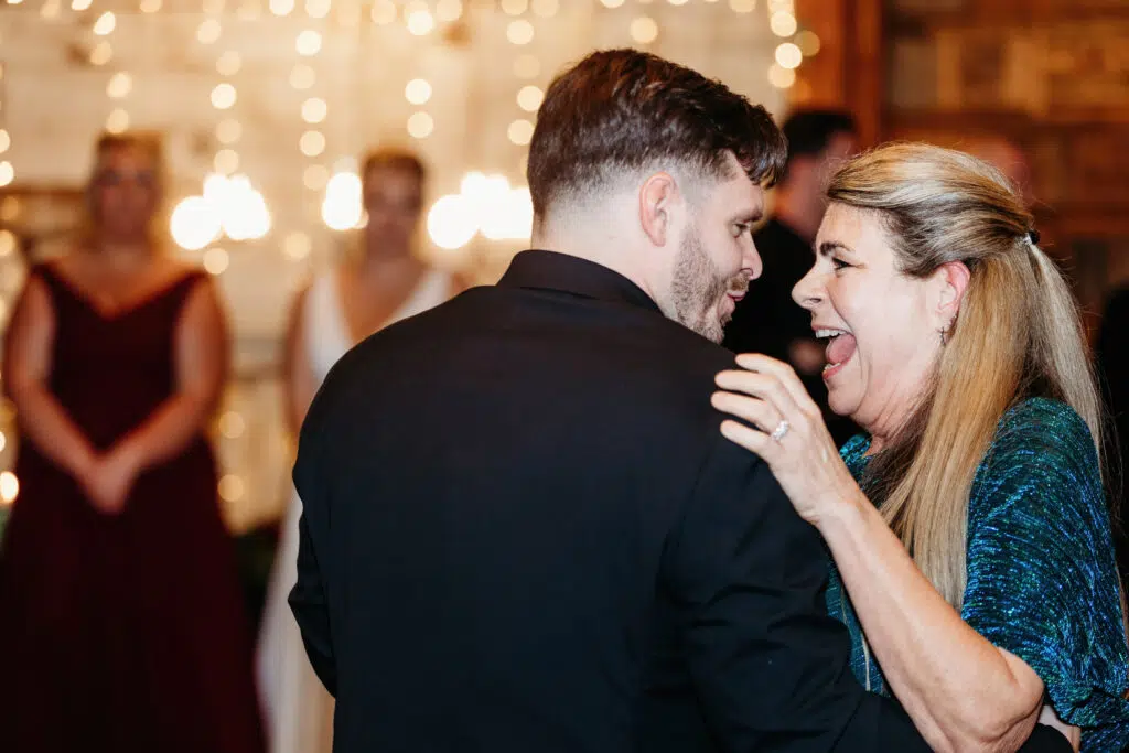 Two people dancing joyfully at an indoor event with soft bokeh lighting in the background, creating a warm and festive atmosphere.