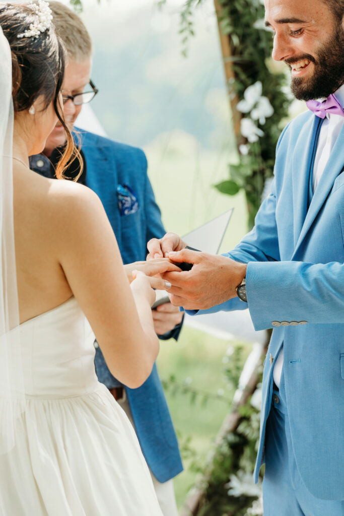 This image shows a wedding ceremony. A person in a blue suit is placing a ring on the finger of a person in a white dress, symbolizing their union.
