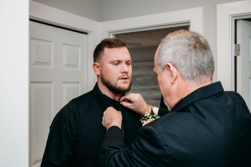 Two men in black shirts stand in a doorway as one adjusts the other's shirt collar.