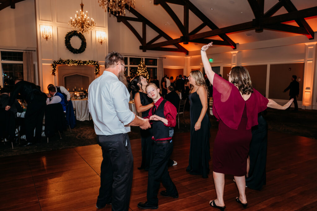 Couples dance in a warmly lit ballroom with a wooden floor and chandeliers.