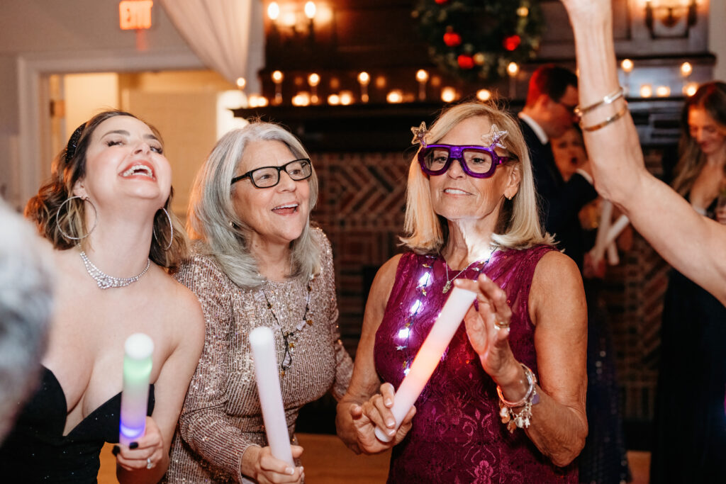 Three people are joyfully holding glowing sticks at a festive indoor event, with candles and decorations in the background.