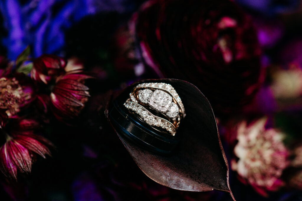 A black hat with a sparkling diamond-studded brooch rests amid dark purple and pink flowers.