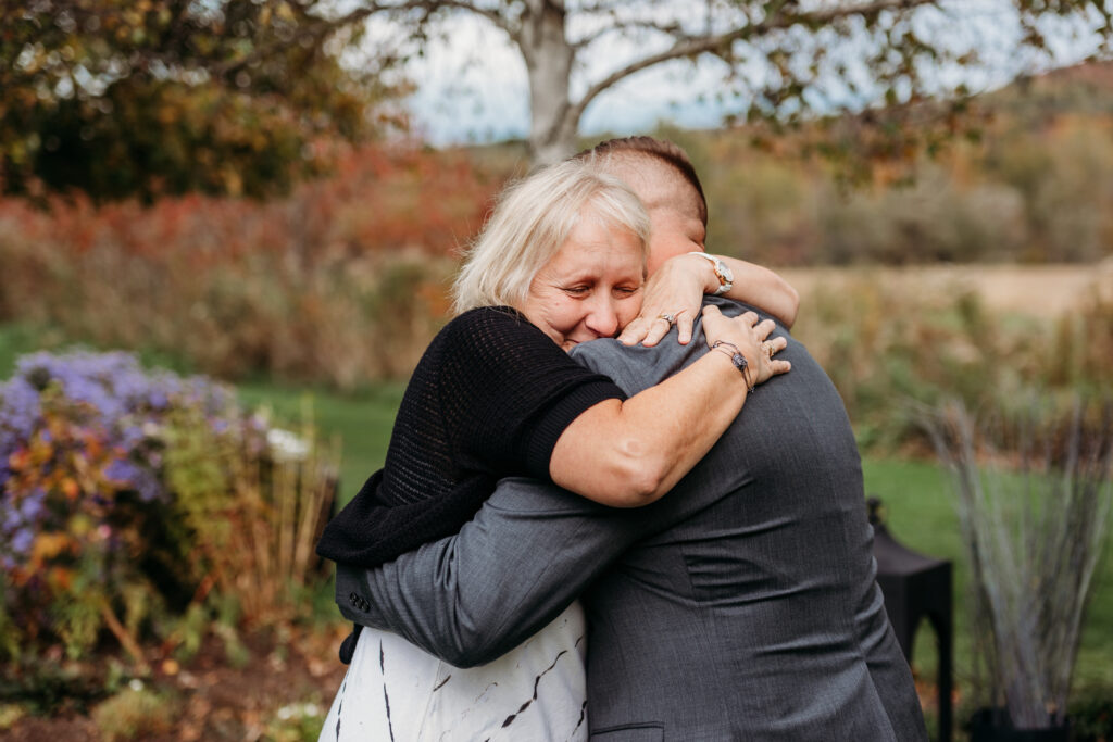 Two people share a warm hug in an autumn garden with colorful flowers.