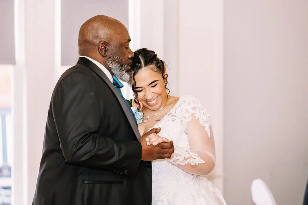 Two people are happily dancing, wearing formal attire. One person is in a black suit, the other in a white lace dress.