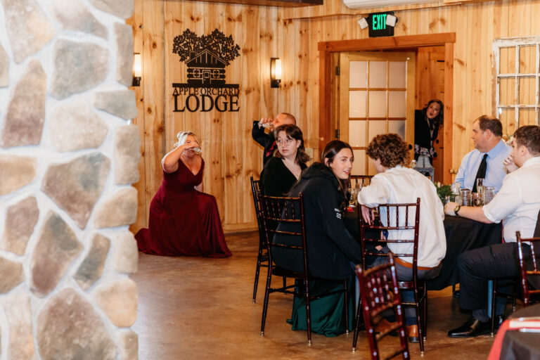 Guests seated at a long table in a rustic lodge with a stone fireplace and wood-paneled walls.