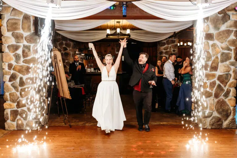 Bride and groom walk hand in hand beneath a draped archway lit by sparklers at their wedding reception.