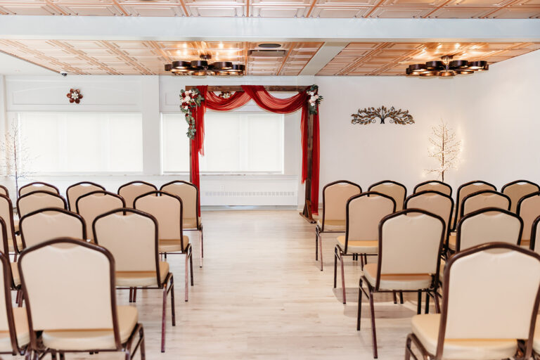 Rows of beige chairs face a small stage with a red curtain arch in a bright ceremony hall.