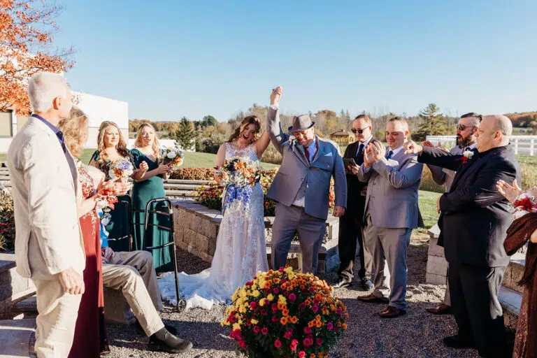 Outdoor wedding ceremony with the bride and groom celebrating as guests applaud, a colorful bouquet in the foreground.