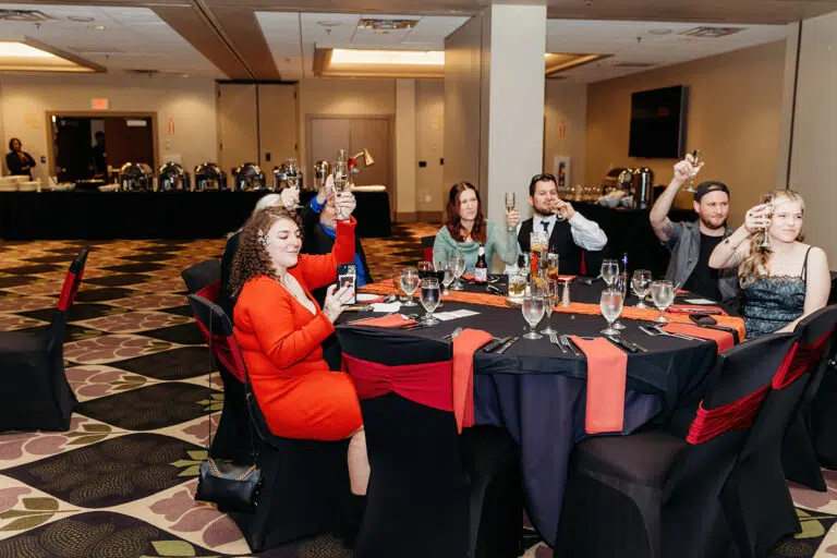 Several guests sit around a round banquet table in a hotel ballroom, posing and smiling at the camera.