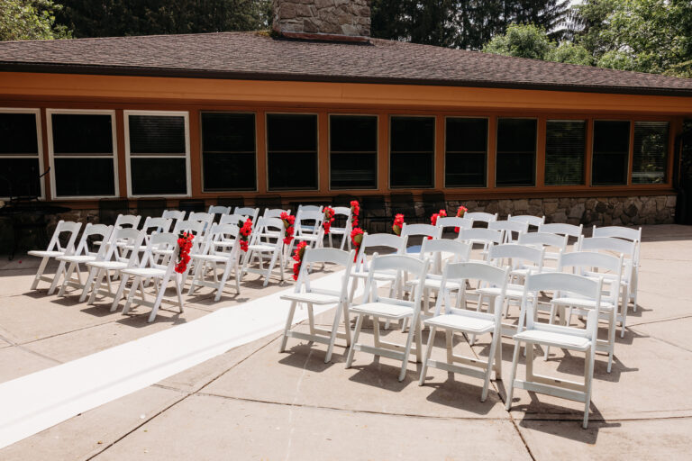 Rows of white folding chairs set up for an outdoor ceremony in front of a brick building.