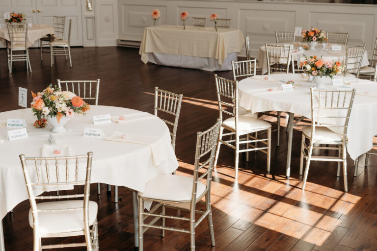 Sunlit banquet hall set for a wedding reception with round tables, white linens, and floral centerpieces.