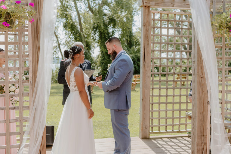 Bride and groom exchange vows under a draped wooden arch during an outdoor wedding.
