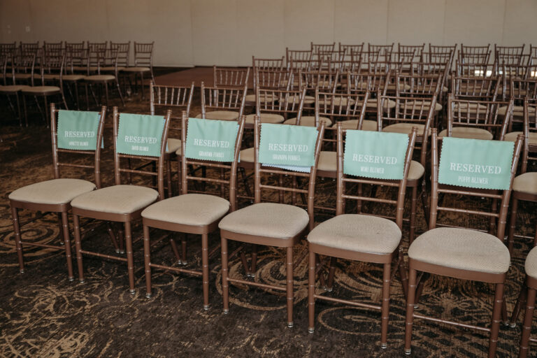 Rows of wooden chairs with light cushions and turquoise back placards in a large room.